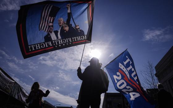 People holding Trump flags silhouetted against bright sun. 