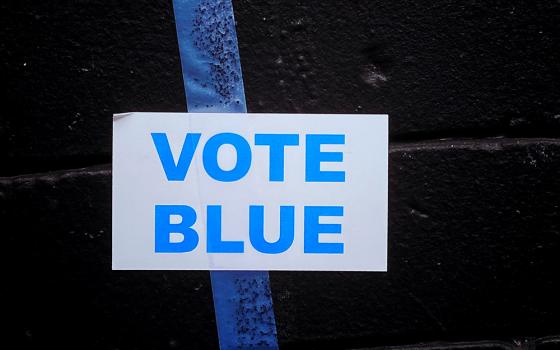 A sign reading "Vote blue" is taped against a black wall. (Unsplash/Jon Tyson)