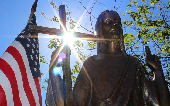 The sun shines through a statue of Christ on a grave marker alongside an American flag at St. Mary Catholic Cemetery in Appleton, Wisconsin, in this 2018 photo. (OSV News file photo/Bradley Birkholz)