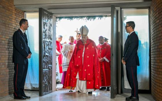 The pope, vested, walks through open double doors. 