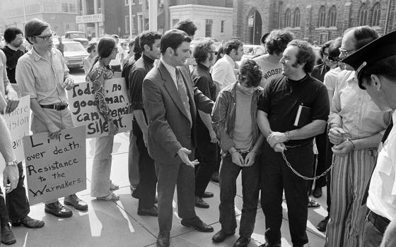 Supporters of persons arrested a week earlier in an attempted raid on a Selective Service office greet those arrested at a court hearing in Camden, New Jersey, on Aug. 30, 1971. Those arrested were brought from a New Jersey jail in handcuffs. Among them is John Grady, right, handcuffed, wearing black.  They became known as the "Camden 28." (AP photo/Bill Ingraham)