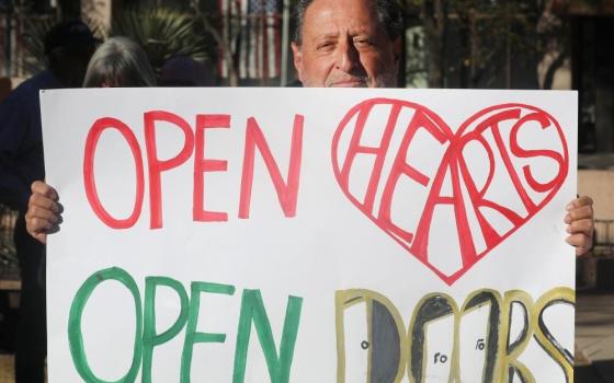 Man holds sign that reads, "Open hearts/open doors."