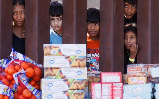 Migrants look through the border fence Sept. 12, 2023, toward food brought by aid workers after gathering between the primary and secondary border fences at the U.S.-Mexico border to wait for processing by U.S immigration officials in San Diego. (OSV News/Reuters/Mike Blake)