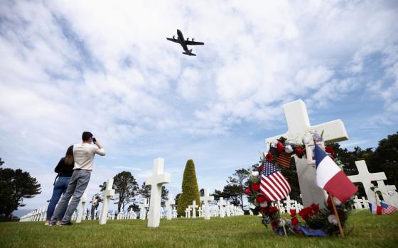People look up as a C-130 aircraft flies over the World War II Normandy American Cemetery and Memorial situated above Omaha Beach during the 77th anniversary of D-Day in Colleville-sur-Mer, France, June 6, 2021. (CNS/Reuters/Stephane Mahe)	 