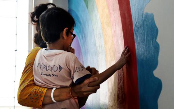 Volunteer with child and rainbow painted on wall.