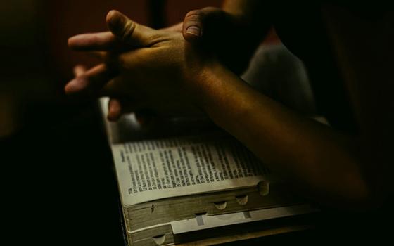 Hands clasped over a bible (Unsplash/Yohan Joy)
