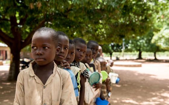 Students at a school in Kandi, Benin, are pictured in a file photo lining up as parent volunteers prepare and serve meals 