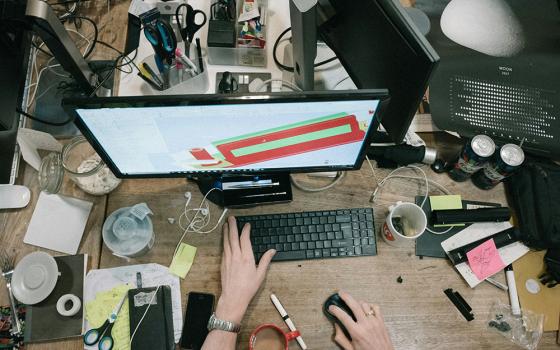 Someone working at a crowded desk on a computer (Unsplash/Robert Bye)