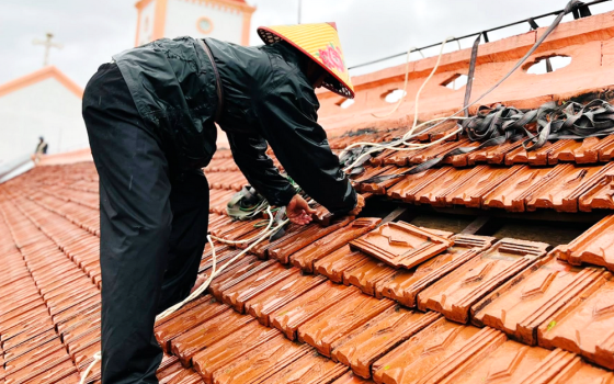 A Lover of the Holy Cross of Hue sister in a raincoat repairs the chapel's damaged roof on Sept. 30, 2025, in Phu Trach commune in Vietnam's Quang Tri province. (GSR photo/Joachim Pham)