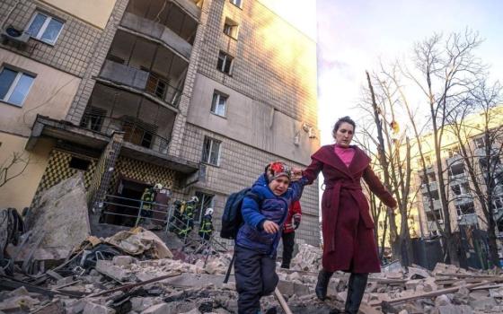 A woman with a child evacuates from a residential building damaged by Russian shelling in Kyiv, Ukraine, March 16. (CNS/Reuters/State Emergency Service of Ukraine)