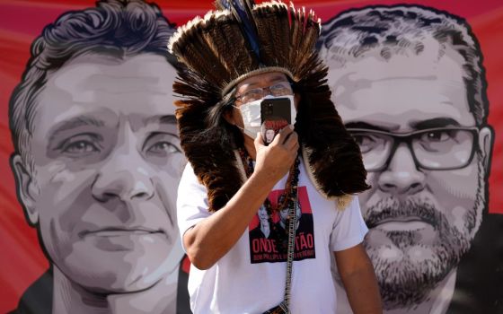 Indigenous leader Kamuu Wapichana stands in front of a banner that show images of missing freelance British journalist Dom Phillips, left, and Indigenous expert Bruno Pereira, during a protest.