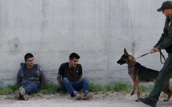 Migrants sit against a levee wall after being apprehended by U.S. Border Patrol agents near Penitas, Texas, on Oct. 8, 2019, after they entered the United States illegally. (CNS/Reuters/Loren Elliott)