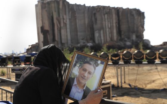 A relative of a victim who was killed in the massive blast last year at the Beirut port reacts and holds his portrait as she attends an Aug. 4 mass held to commemorate the first year anniversary, at the Beirut port, Lebanon. (AP/Hussein Malla)