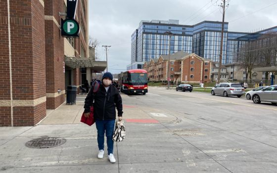 Man in a mask walking along a sidewalk toward camera