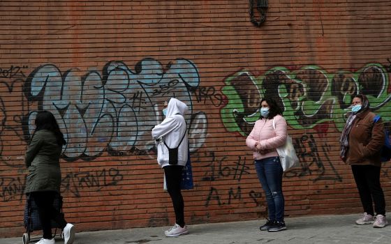 People in masks wait in line to receive donated food