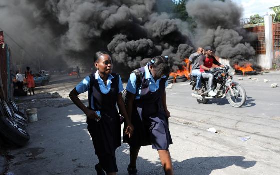 Schoolgirls walk past a burning street barricade during demonstrations Nov. 25, 2021, against widespread kidnappings in Port-au-Prince, Haiti. (CNS/Reuters/Ralph Tedy Erol)