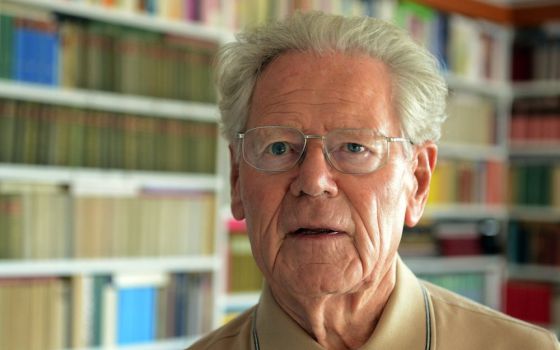 White haired man in glasses in front of books on a shelf