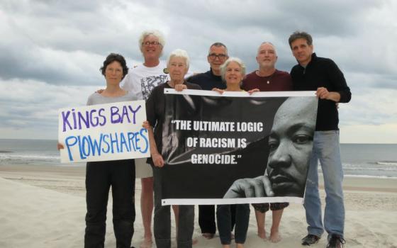 Seven people on a beach holding signs; one says "Kings Bay Plowshares," the other features a portrait of Martin Luther King, Jr. 