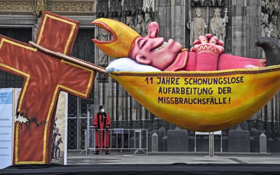 A carnival float depicting a sleeping Cardinal, reading '11 years of relentless processing of cases of abuse' is set in front of the Cologne Cathedral to protest against the Catholic Church in Cologne, Germany, Thursday, March 18, 2021. (AP Photo/Martin M