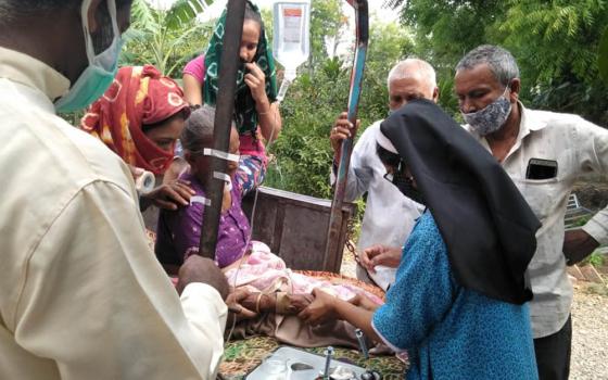 Fr. Ajeesh Chirayarikil, left foreground, helps Sr. Lisset Vadakkekara, at right in blue, administer an IV drip to a woman with COVID-19 symptoms in front of Jyoti clinic, managed by Congregation of Mother Carmel nuns at Chachana village in Gujarat, India