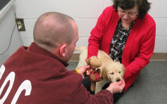 Benedictine Sr. Sue Fazzini and an inmate at the Pennsylvania State Correctional Institution Greene play with a puppy in training for Canine Partners for Life, a Chester County, Pennsylvania-based organization dedicated to training service dogs, home comp