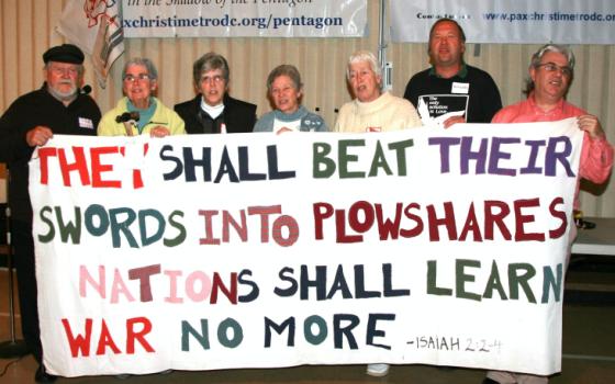 Seven plowshares activists seen together at the Pax Christi event Sunday. They are holding a sign created by the late Philip Berrigan, who participated in the first action in 1980. (Photos courtesy of Ted Majdosz)