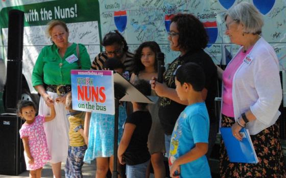 Katherine Meza, second from right, tells the crowd gathered in front of St. Anthony Church about how she and her five younger siblings are under the care of their grandmother, standing left, in green, after their parents were deported to Honduras in May. Social Service Sr. Simone Campbell, right, offers comfort during the emotional story. (GSR photo / Dawn Cherie Araujo)