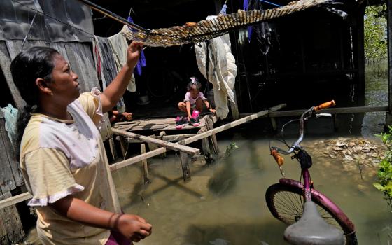 Nia Riningsih checks salted fish she dries as her daughter Safira plays at their house in Mondoliko village, Central Java, Indonesia, Sunday, Nov. 7, 2021. (AP/Dita Alangkara)