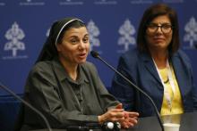 A brown nun speaks into a microphone while a brown woman in Western business clothes sits beside her