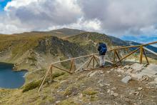 A person stands before a wooden barrier in a landscape with mountains and a lake (Unsplash/Luba Ertel)