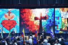 People stand on stage; behind stage are illuminated panels of mosaic-style images. 