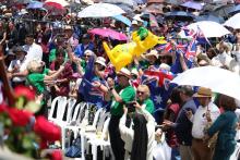 Many people stand from plastic chairs cheering and waving flags etc.