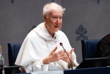 Radcliffe wearing white habit of the Dominicans, sits at table speaking.