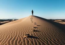 A person stands on top of a sand dune, with sunlight coming from the left of the photo.(Unsplash/NOEM)