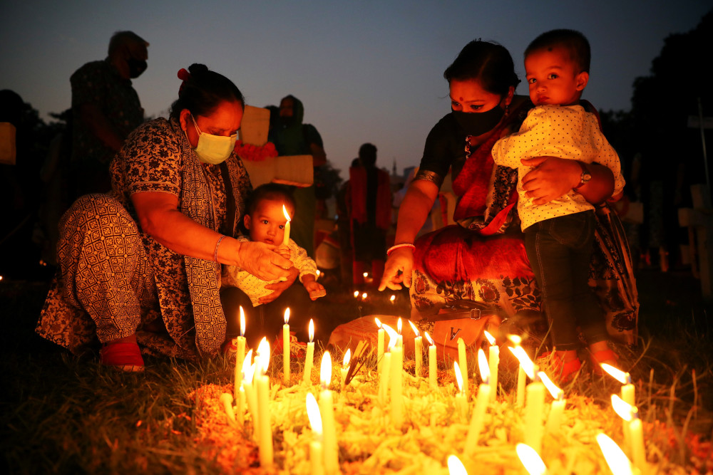 A woman helps a child to light a candle as they pray for the departed souls of their relatives at a cemetery in Dhaka, Bangladesh, during the feast of All Souls Nov. 2, 2021. (CNS/Reuters/Mohammad Ponir Hossain)