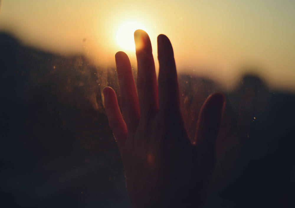 Hand smudging a glass window, backlit by a warm sunset shining through fingers