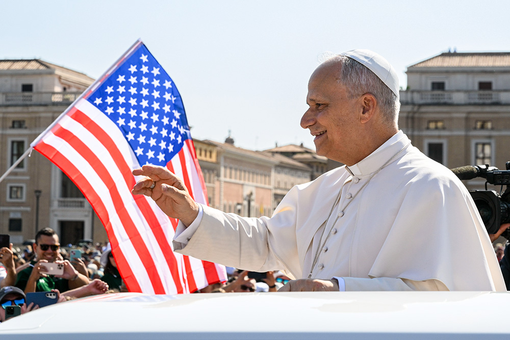 With a U.S. flag in the background, Pope Leo XIV waves to the crowd from the popemobile as he rides around St. Peter's Square at the Vatican before his weekly general audience Aug. 6, 2025. (CNS/Vatican Media)