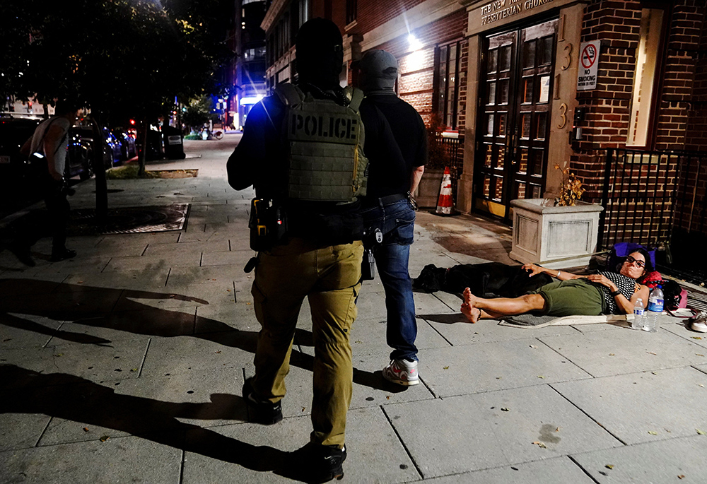 Members of federal law enforcement walk past a homeless woman outside of a church in Washington Aug. 14, 2025, following President Donald Trump's announcement of the federal takeover of the Metropolitan Police Department under the Home Rule Act and the deployment of the National Guard in the nation's capital. (OSV News/Reuters/Nathan Howard)