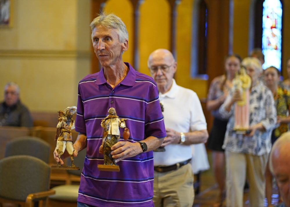 Joe Loney carries two figurines as he participates in the presentation of the gifts during a Mass Aug. 16.