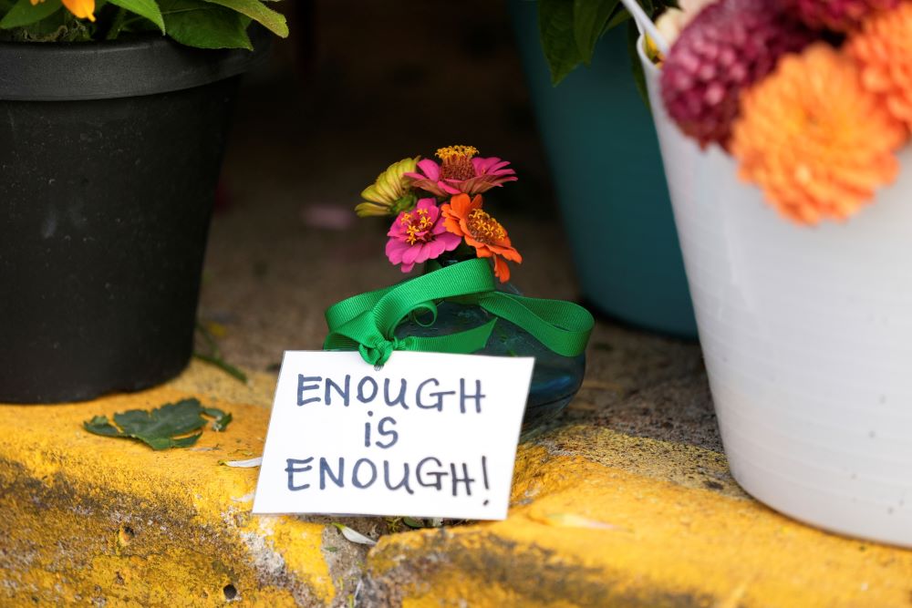 A sign reading "Enough is enough" stands amid flowers at a memorial at Annunciation Catholic Church.