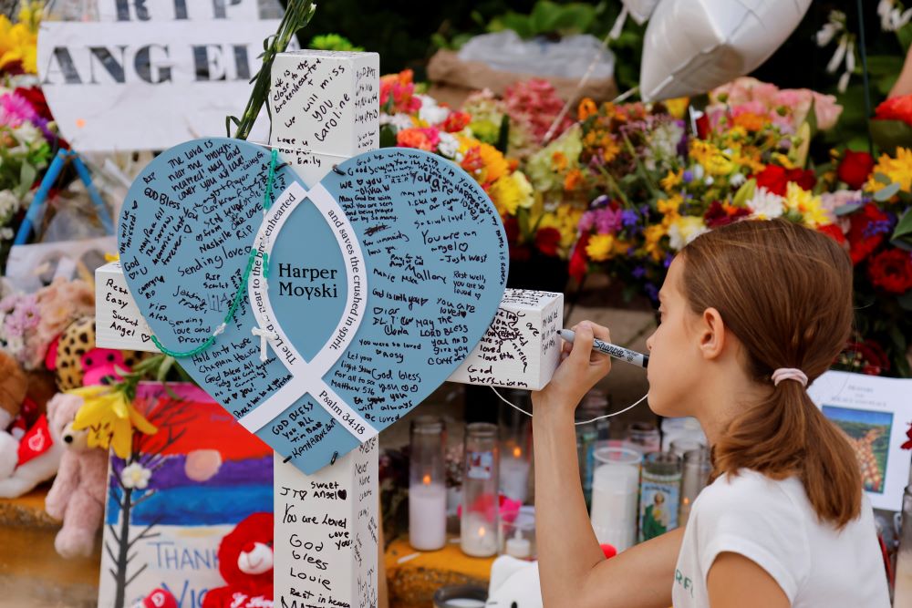 A child writes a message as people at a makeshift memorial. 
