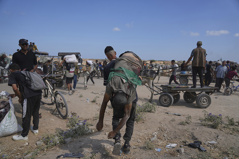 A Palestinian carries the body of a man killed while trying to receive aid near a distribution center operated by the U.S.-backed Gaza Humanitarian Foundation (GHF) in Netzarim, in the Gaza Strip, Aug. 4, 2025. (AP Photo/Abdel Kareem Hana)