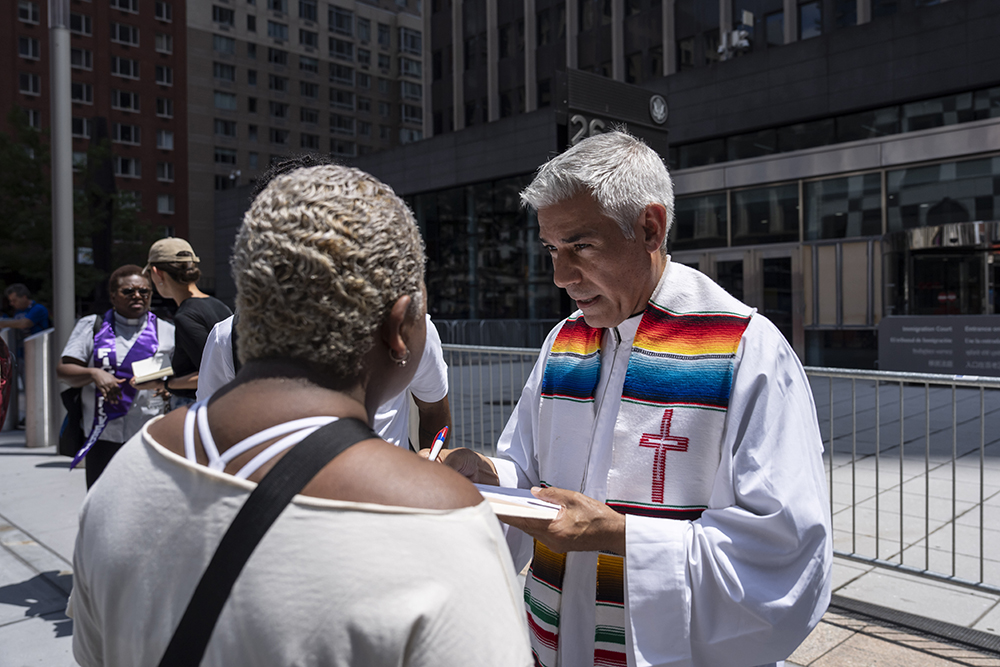 Fr. Fabián Arias, right, assists an immigrant family outside the Jacob K. Javits federal building, July 17, 2025, in New York. (AP/Yuki Iwamura)