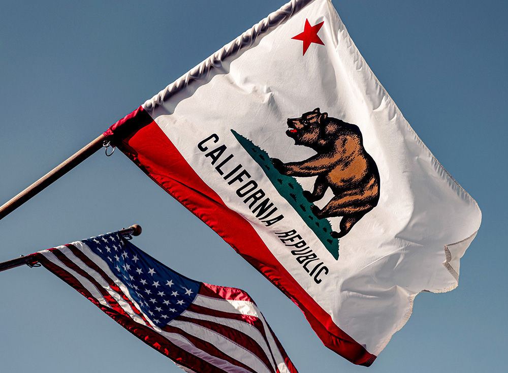 The U.S. flag and the California state flag are seen flying in Santa Barbara, California. (Unsplash/Tim Mossholder)