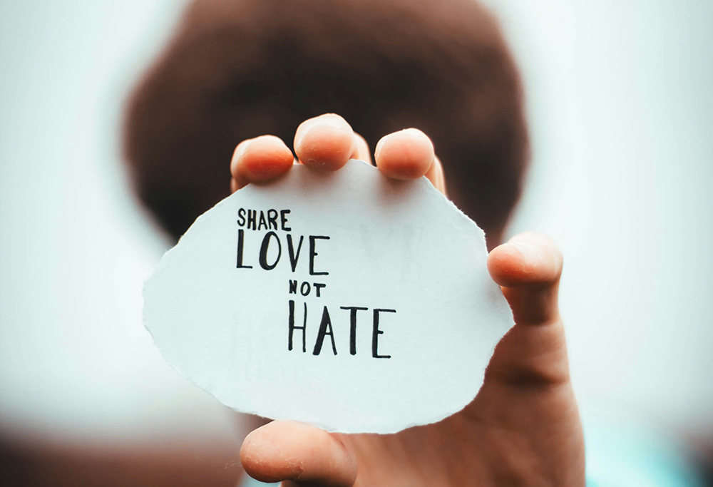 A person holds up a paper with "Share love not hate" written on it (Unsplash/Dan Edge)