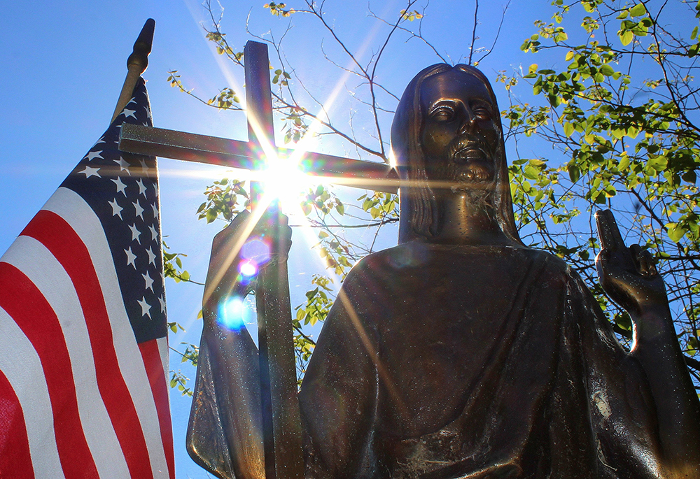 Sun shines through a statue of Jesus Christ on a grave marker alongside an American flag at St. Mary Catholic Cemetery in Appleton, Wisconsin, in this 2018 photo. (OSV News/Bradley Birkholz)