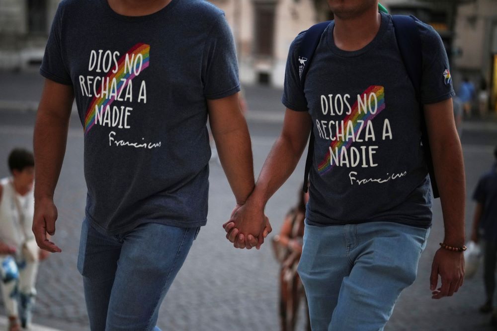  Two people hold hands and wear T-shirts reading "God does not reject anyone" in Spanish.