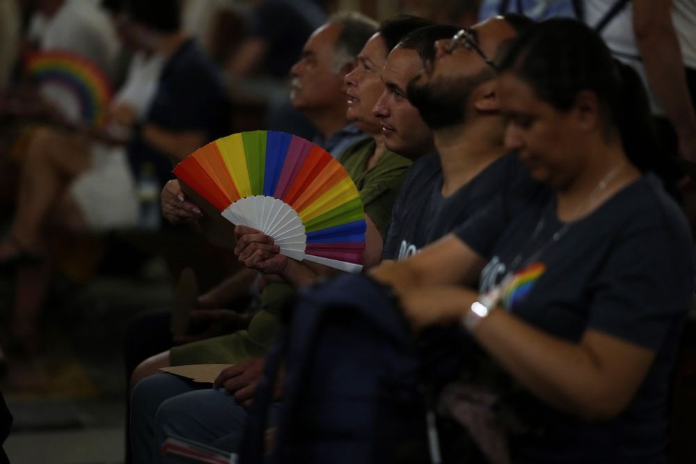 Members of the LGBTQ+ community, one holding a rainbow fan, attend a vigil prayer. 