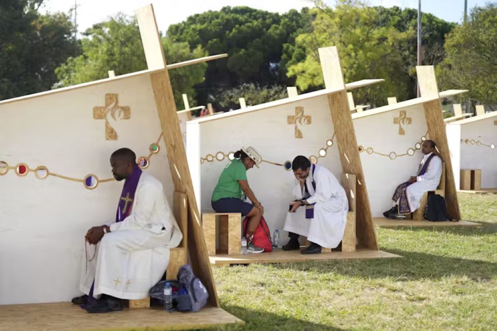 A priest listens to confession in a row of confessionals set up for pilgrims during World Youth Day in Lisbon, Portugal, on Aug. 1, 2023. (The Conversation/AP/Ana Brigida)