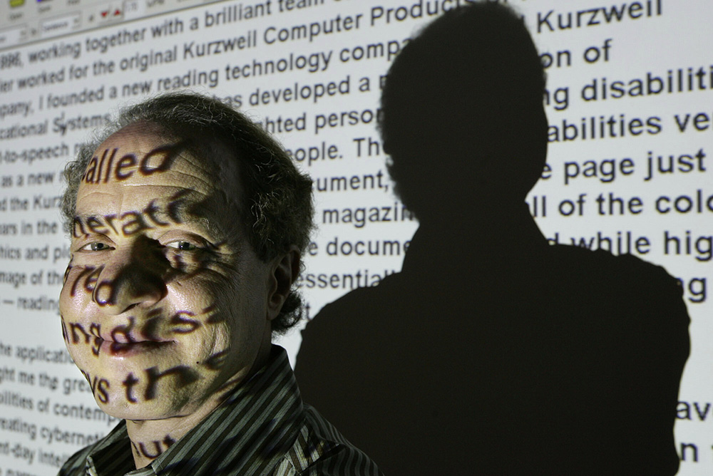 Ray Kurzweil stands for a portrait in front of words from his website projected on a screen in his office in Wellesley, Mass., Jan. 12, 2005. (AP/Steven Senne, File)